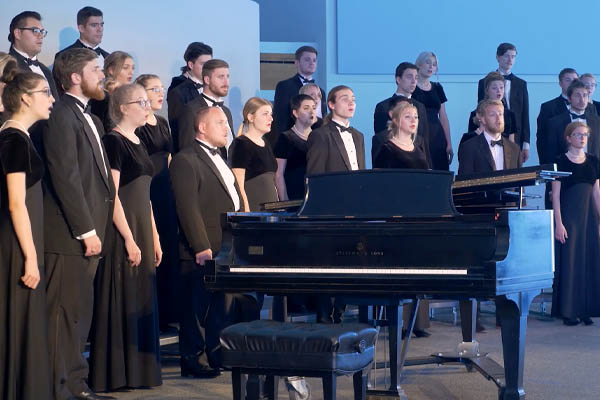 choir singing around a piano