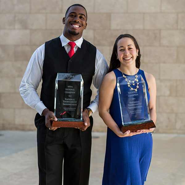 Male and female student holding forensics trophies
