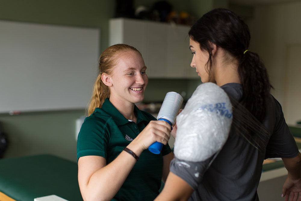 A volleyball player gets her shoulder wrapped by an athletic trainer.