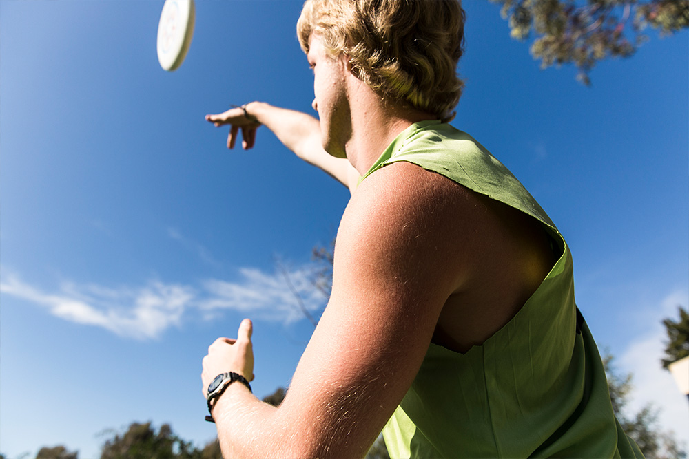 A student makes an overhand toss to his teammate in a game of ultimate frisbee.