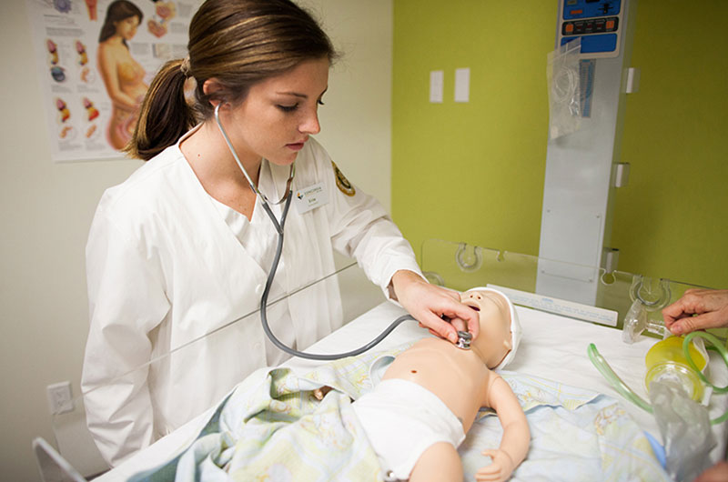 Nursing student checking the heartbeat of a manikin patient baby