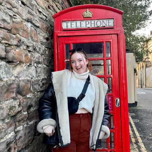 A woman poses by a vibrant red phone booth, a city staple.