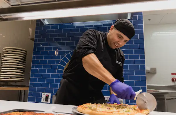 Cafteria worker cutting pizza