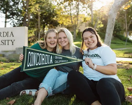 Three female Concordia students holding a school flag