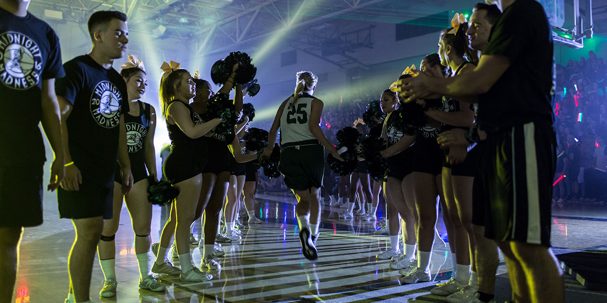 Athletes enter the gym surrounded by cheer leaders and team members