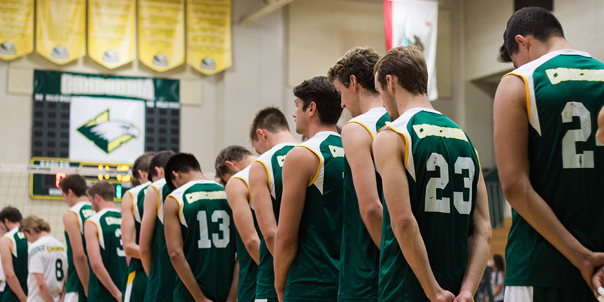 CUI men's volleyball players bowing their heads for prayer before a game