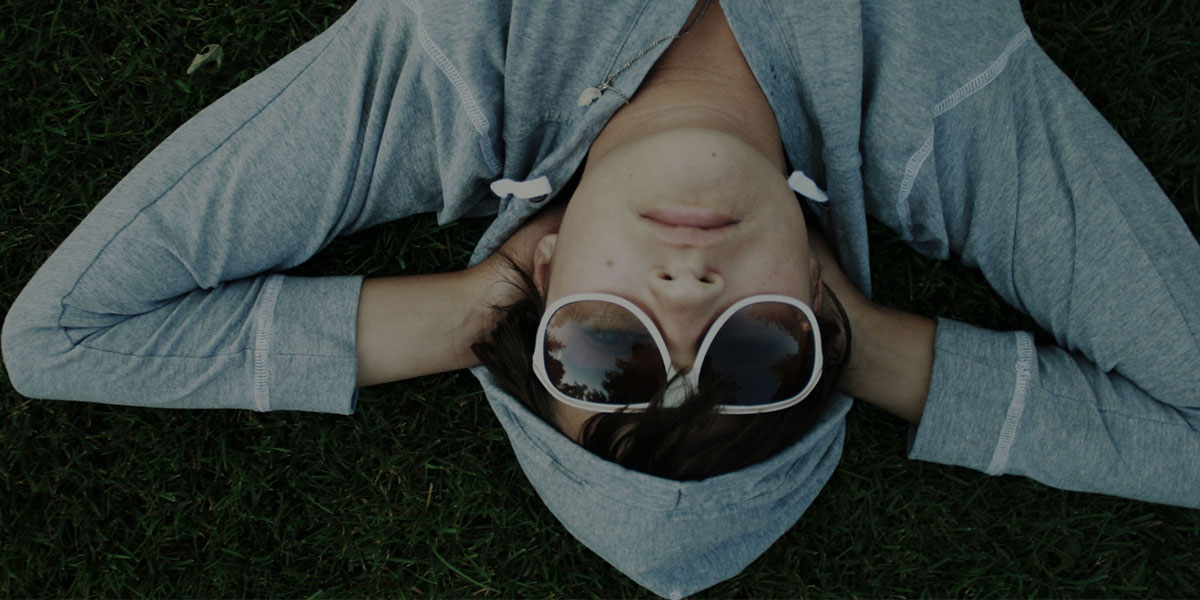Boy with sunglasses and hoodie laying in the grass