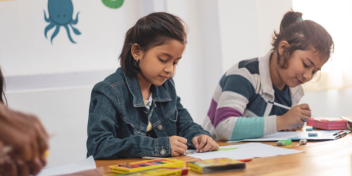 Two girls in a classroom writing.