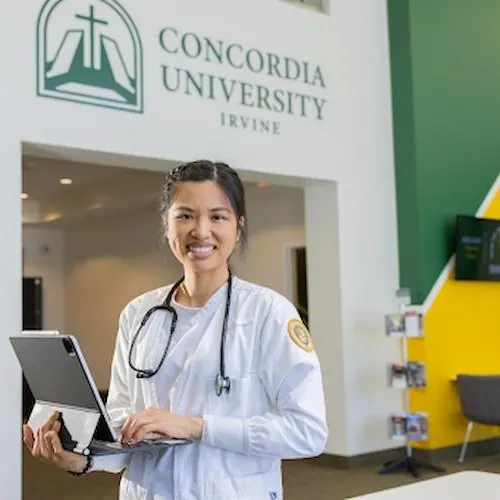 A nurse smiling and holding a laptop at Concordia University Irvine