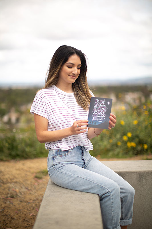 Natalie Cervantes sitting holding a holiday card she designed