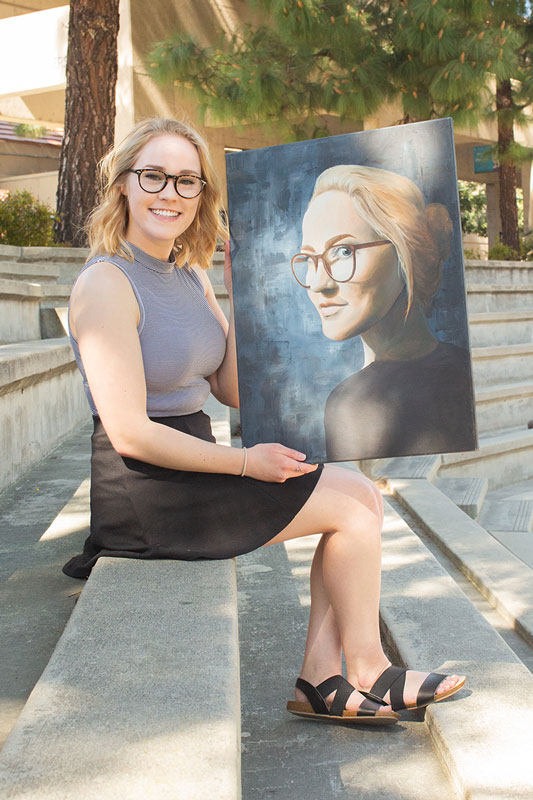 Sami Newport sitting with a self-portrait painting on canvas