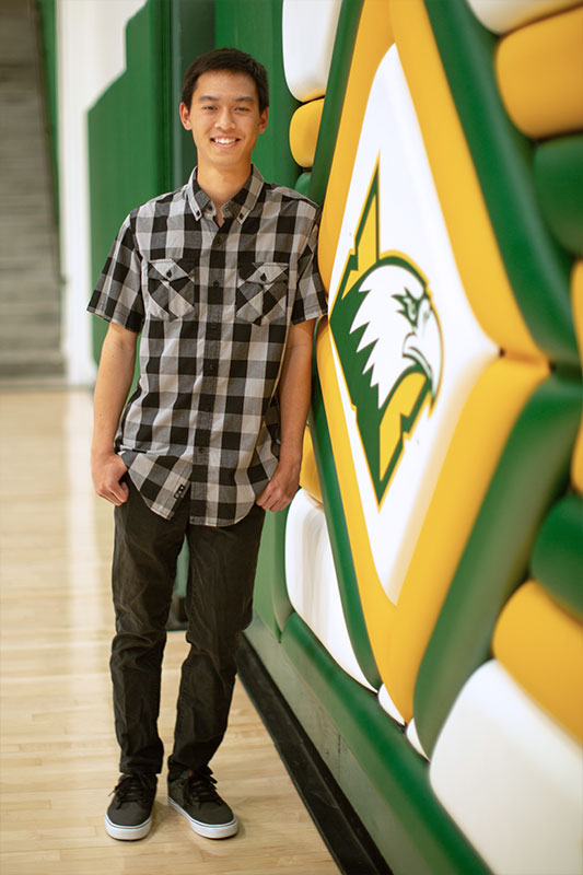 Troy Makalena leaning against a wall with the CUI Eagles logo