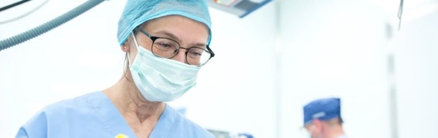 Nurse in surgical scrubs, cap and mask preparing anaesthesia equipment
