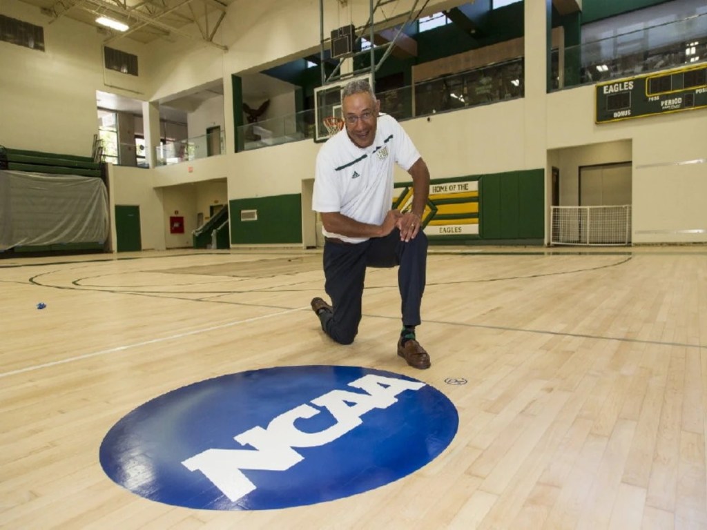 A man kneeling behind the NCAA logo at the Concordia gym