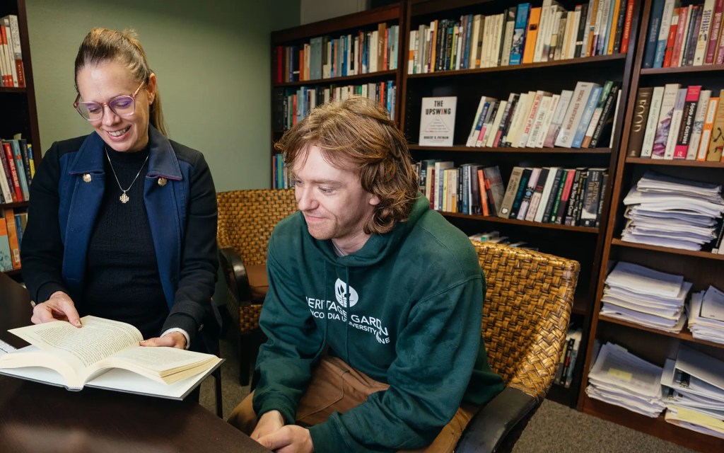 A man and woman sitting at a table with books in the background