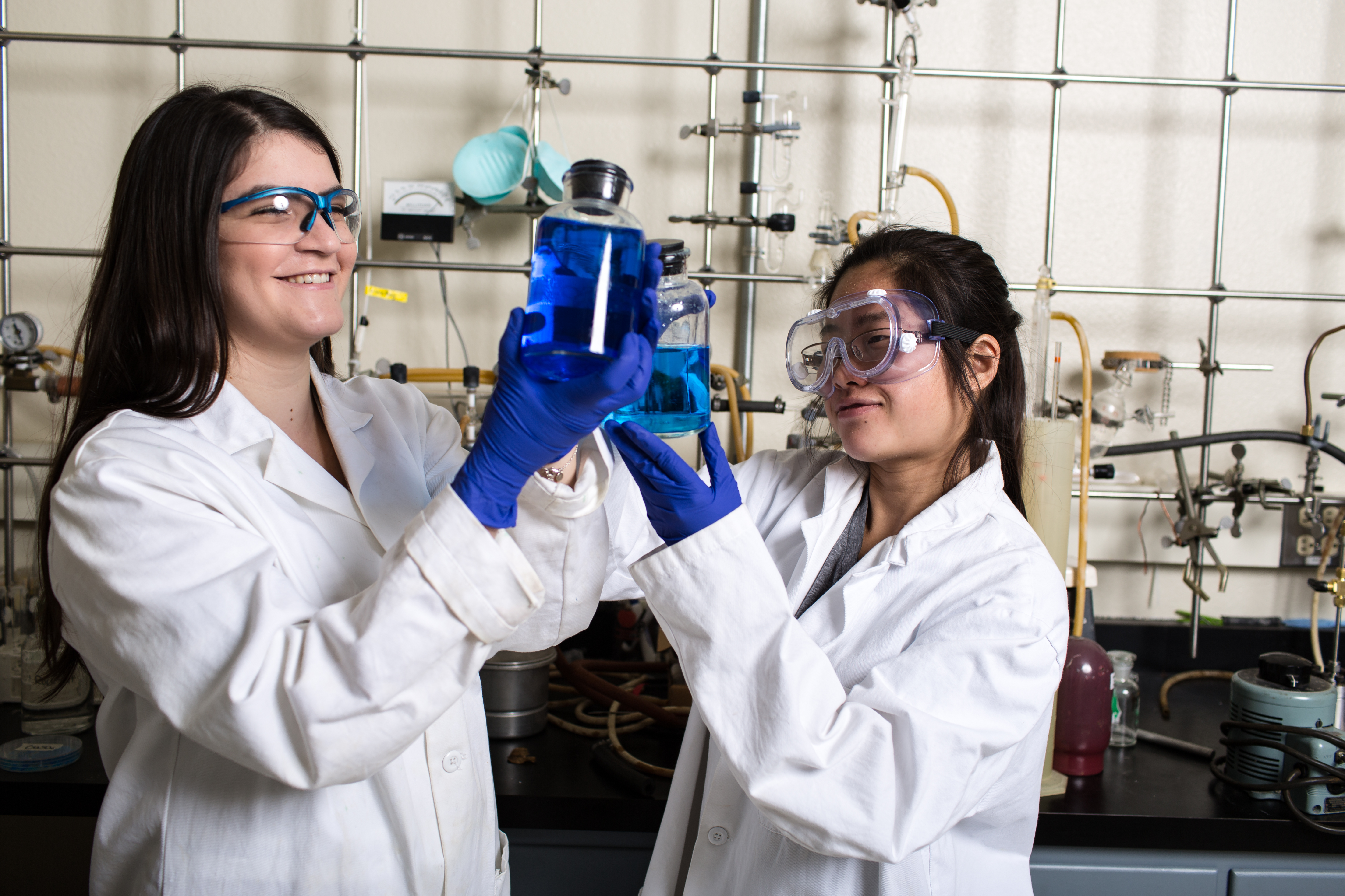 Two women in white lab coats holding blue liquid