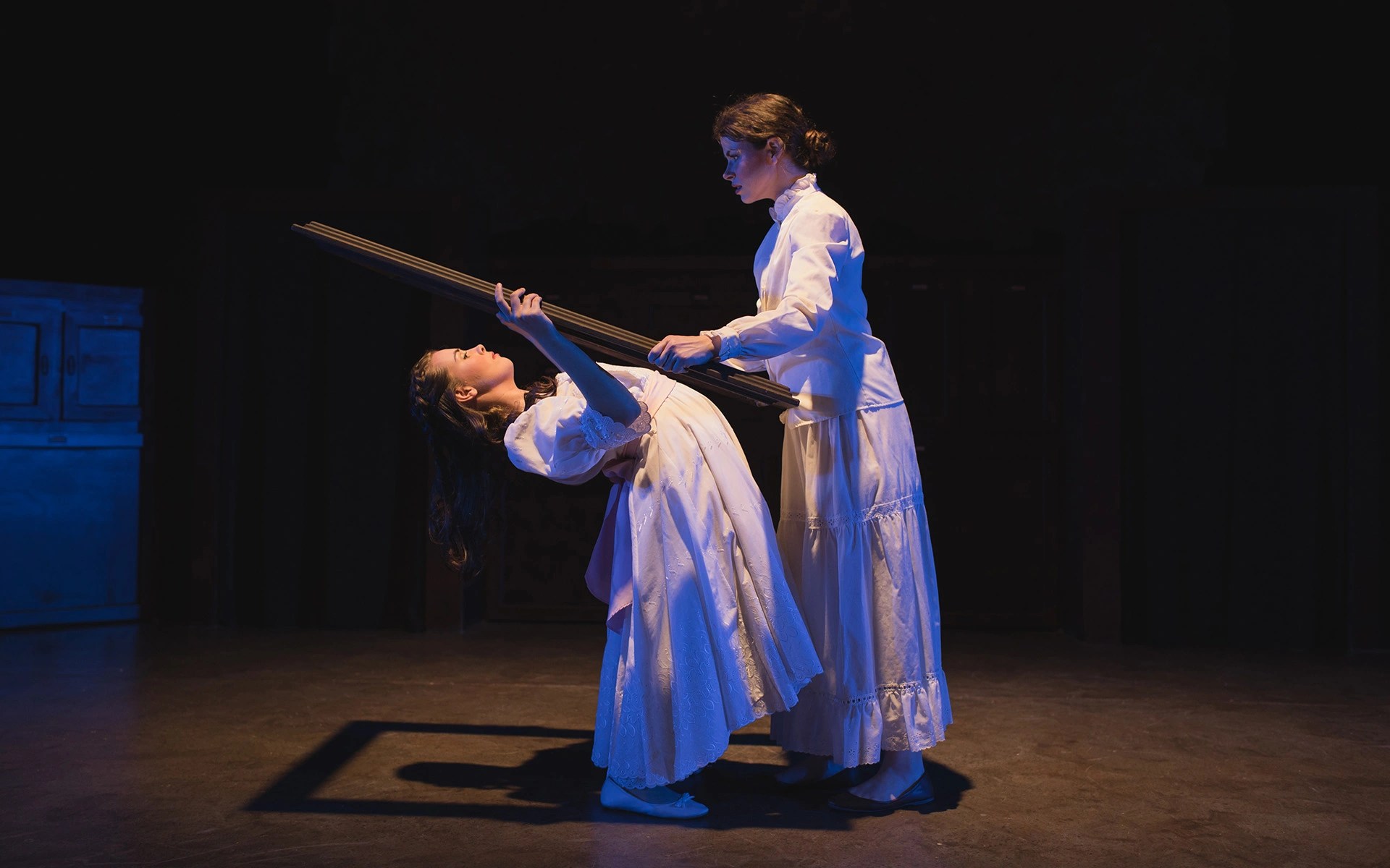 Two women in white dresses holding a pole