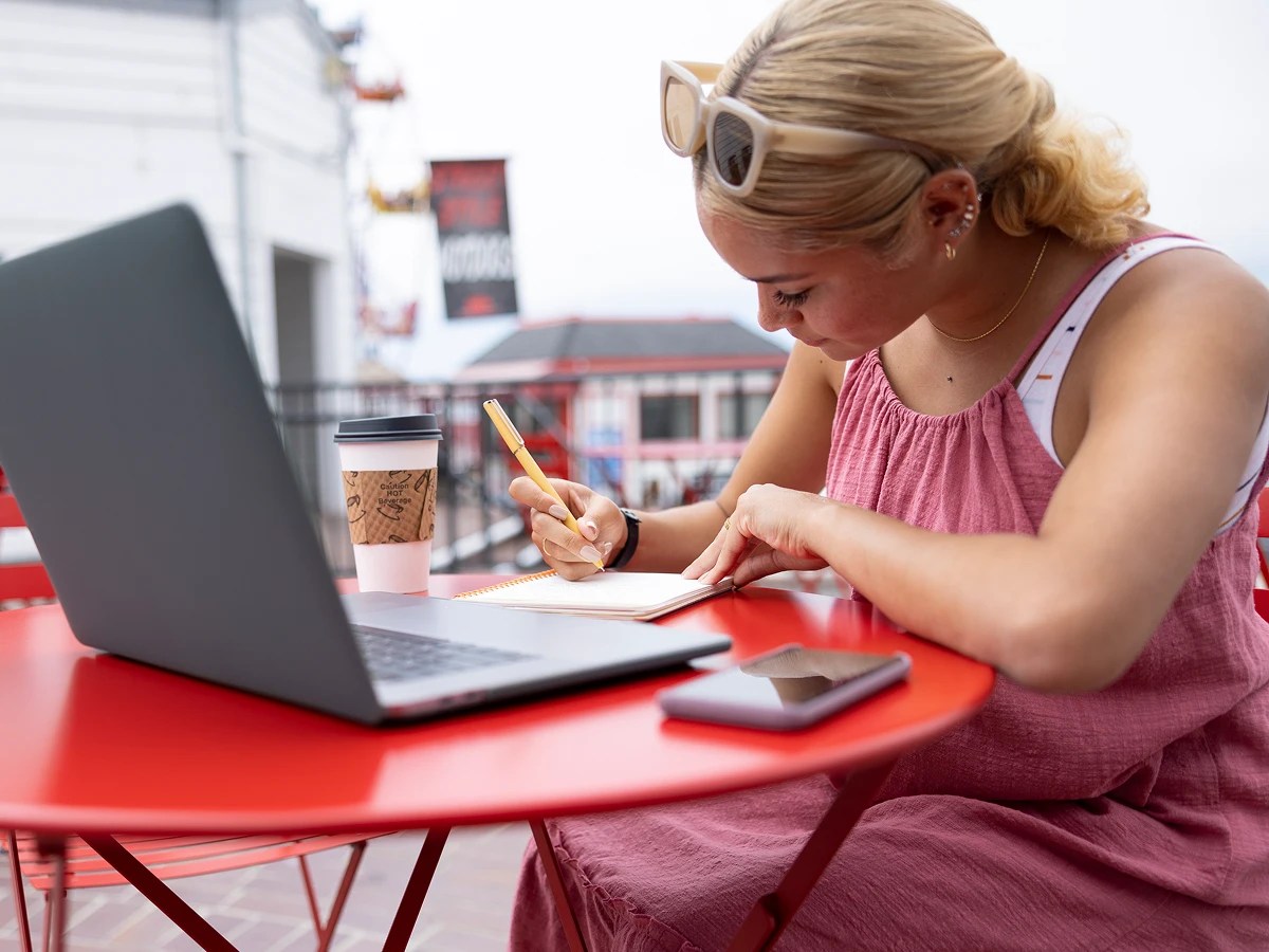 A woman sitting at a red table with a laptop and a phone