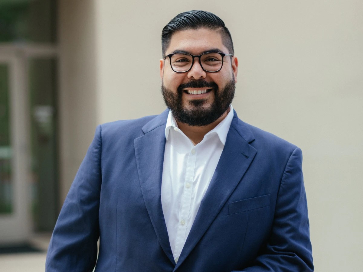 Man in a blue suit smiling outdoors in a professional portrait setting