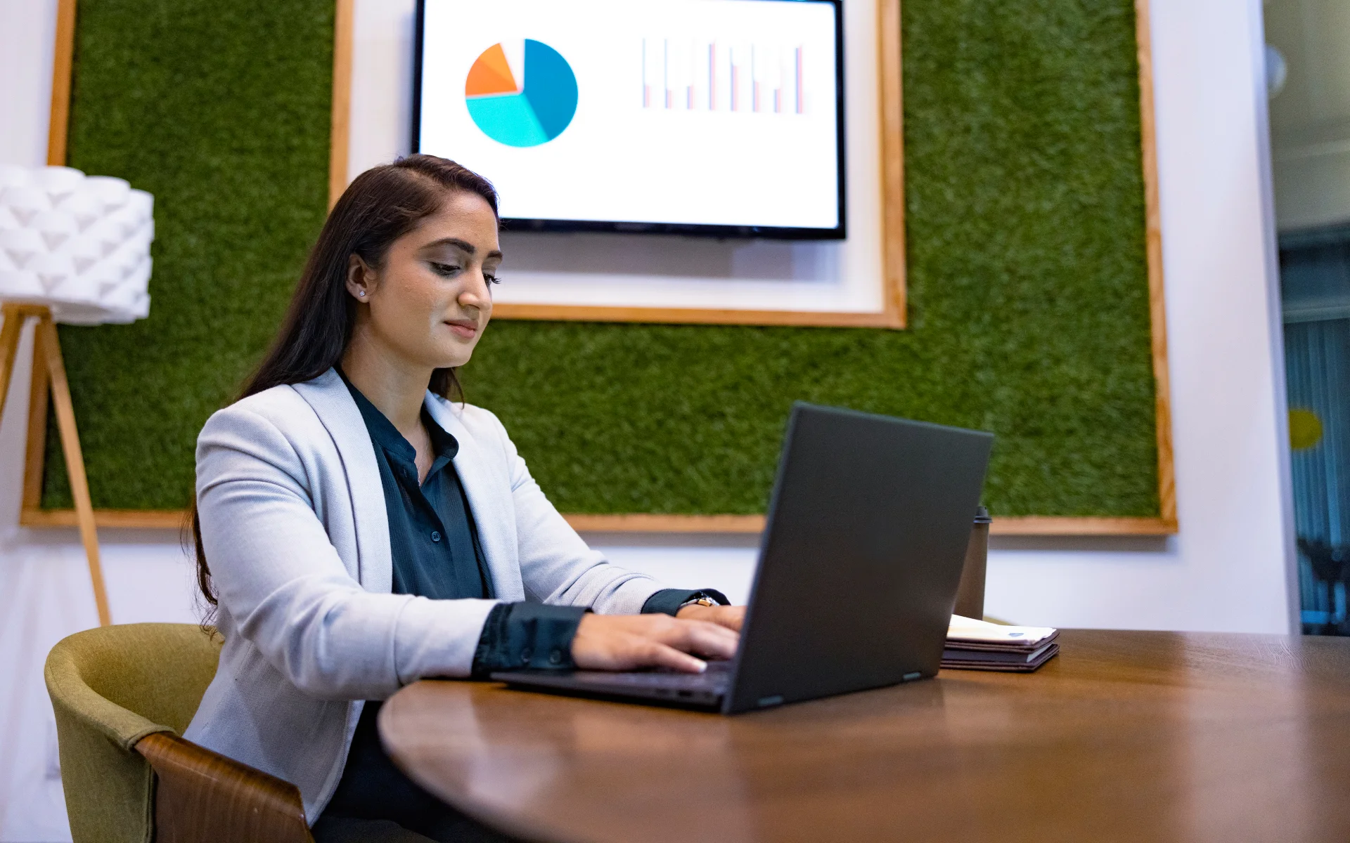 Business student working on a laptop with charts displayed on a screen in the background