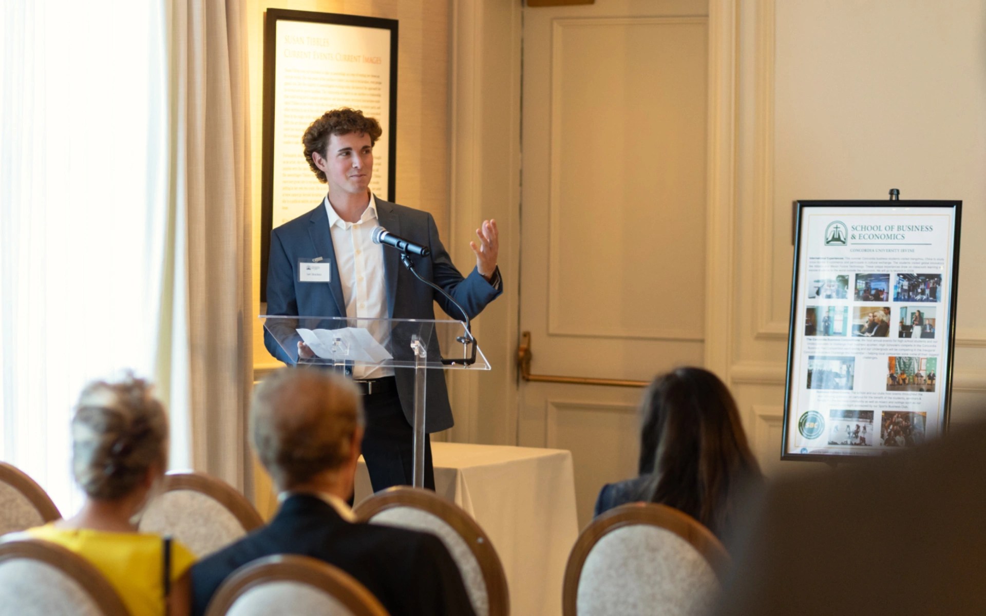 Student in a suit speaking at a podium during a School of Business and Economics event with an audience seated