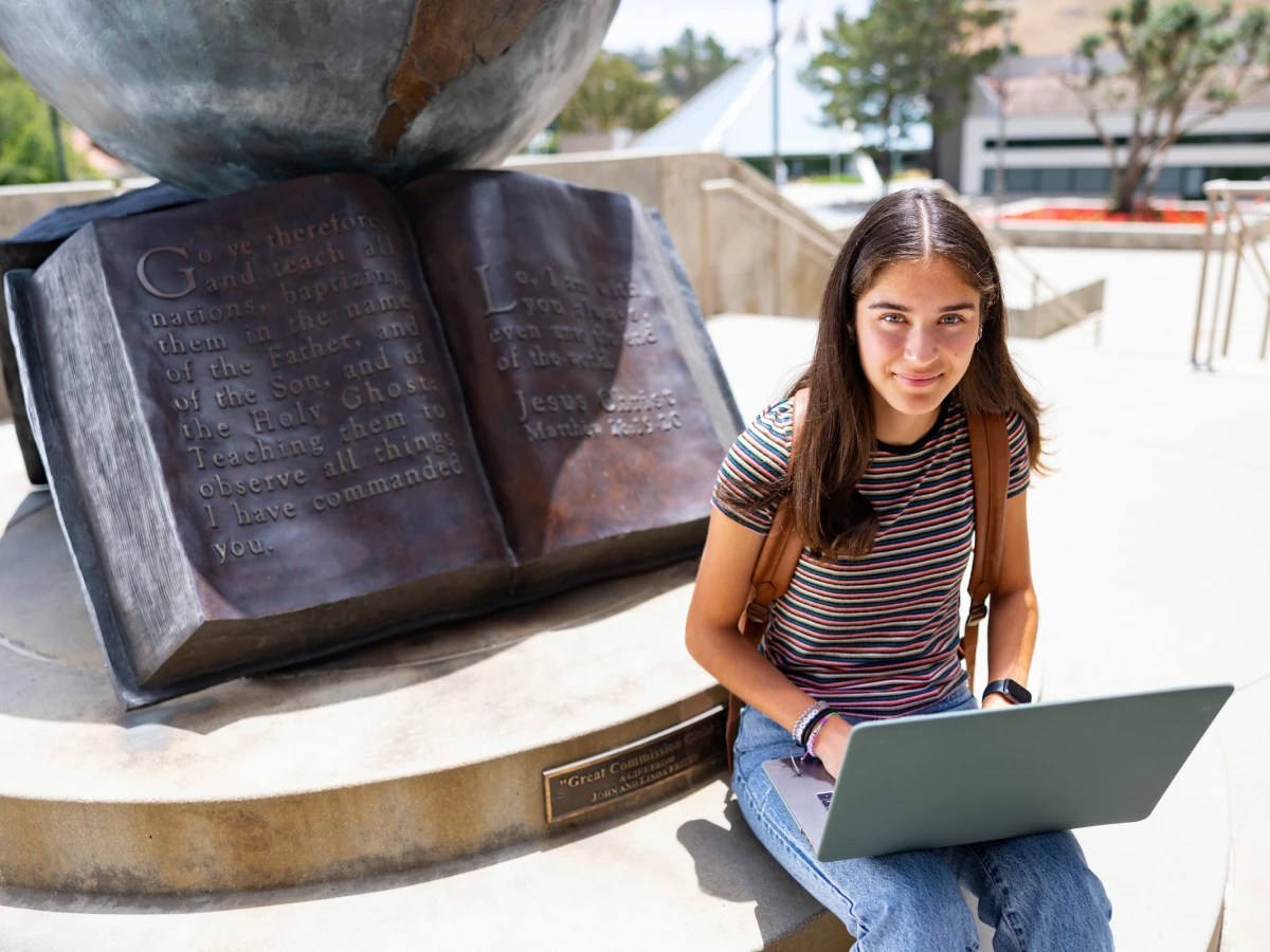 A woman sitting on a stone bench with a laptop