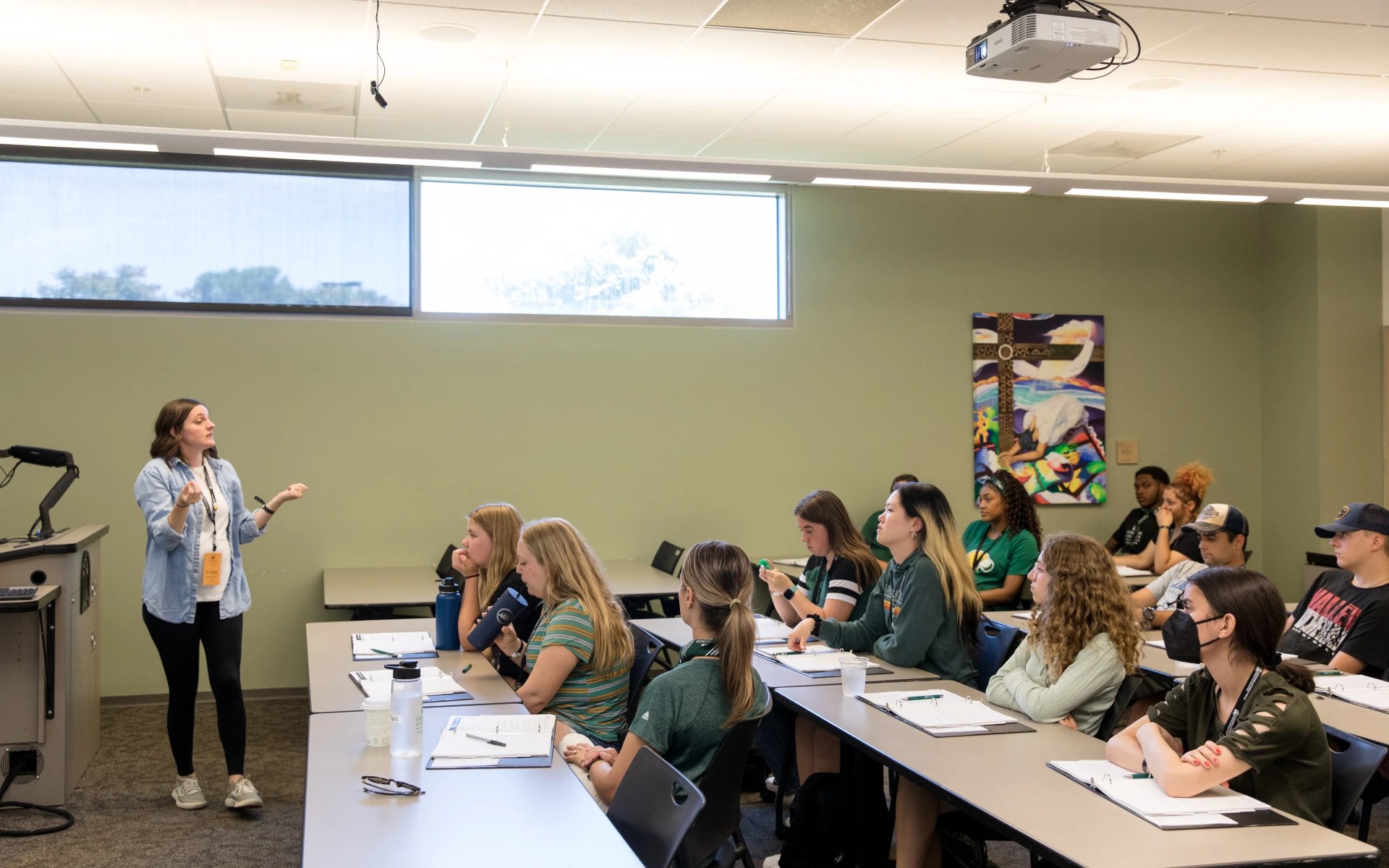 Instructor speaking to a classroom of college students attentively listening and taking notes during a lecture