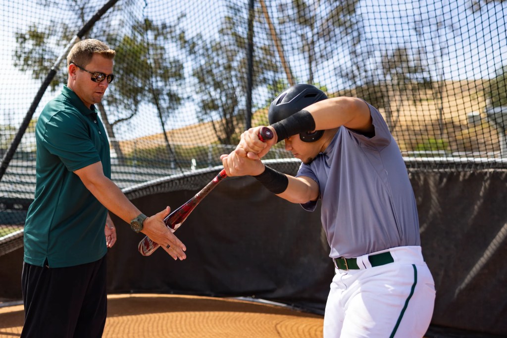Concordia University Irvine baseball coach training a student athlete at the batting cage