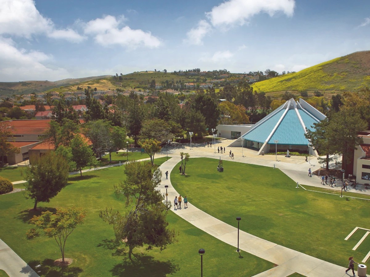 Aerial view of Concordia University Irvine’s central lawn with walkways, trees, and the distinctive blue-roofed CU Center, with surrounding hills in the background
