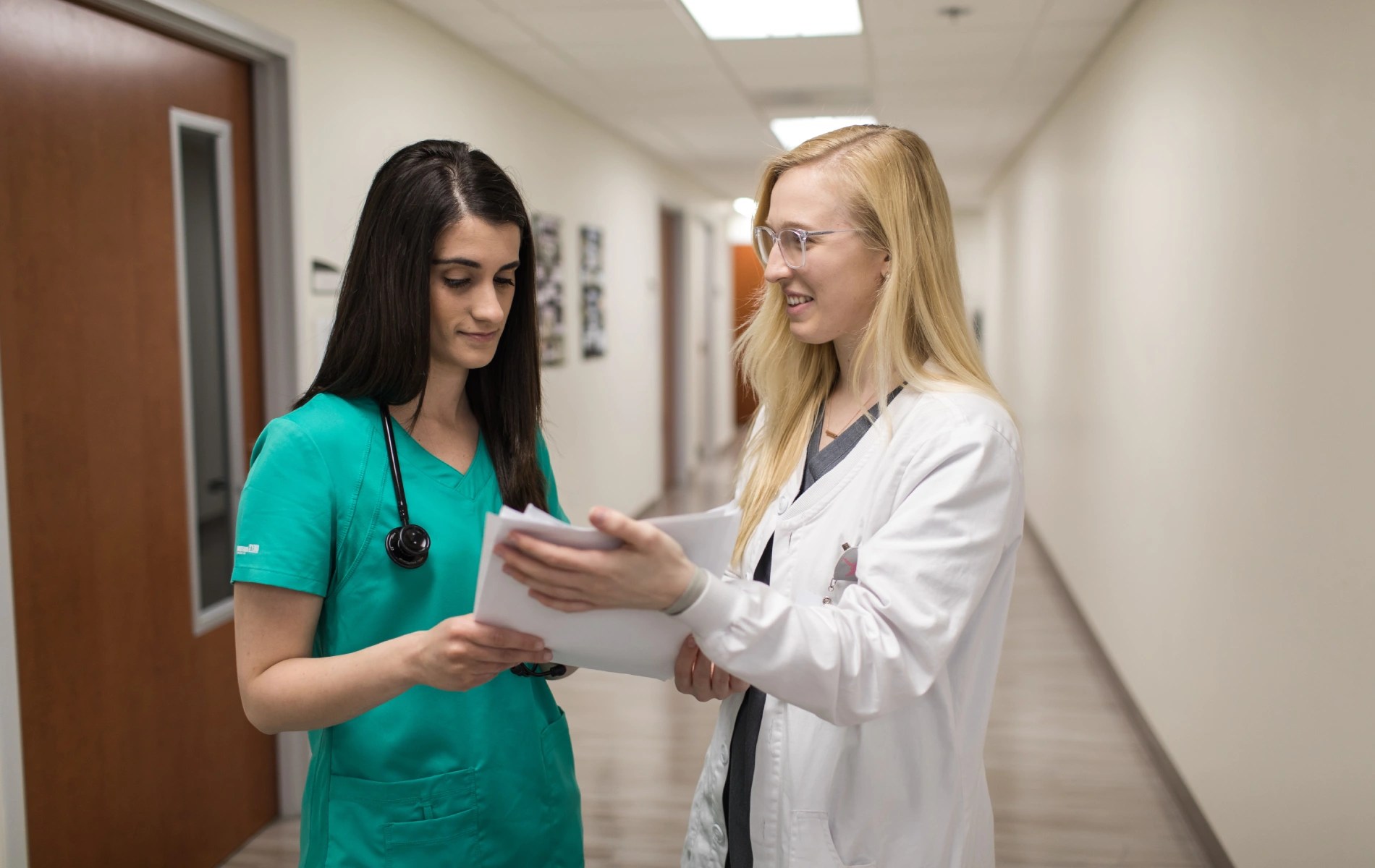 Two people in medical uniforms standing in a hallway reviewing papers