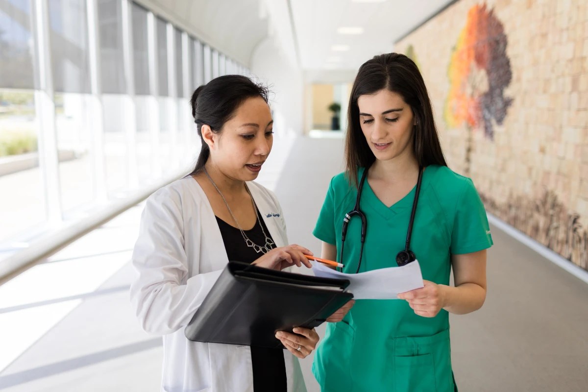 Concordia University Irvine nursing faculty member mentoring a nursing student in scrubs while reviewing patient notes in a hospital hallway