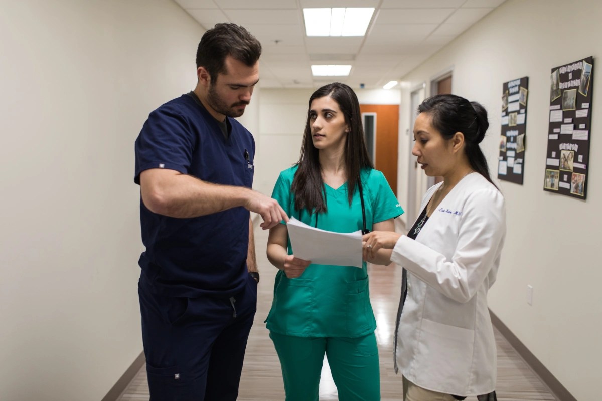 Three people in medical uniforms discussing a document in a hallway