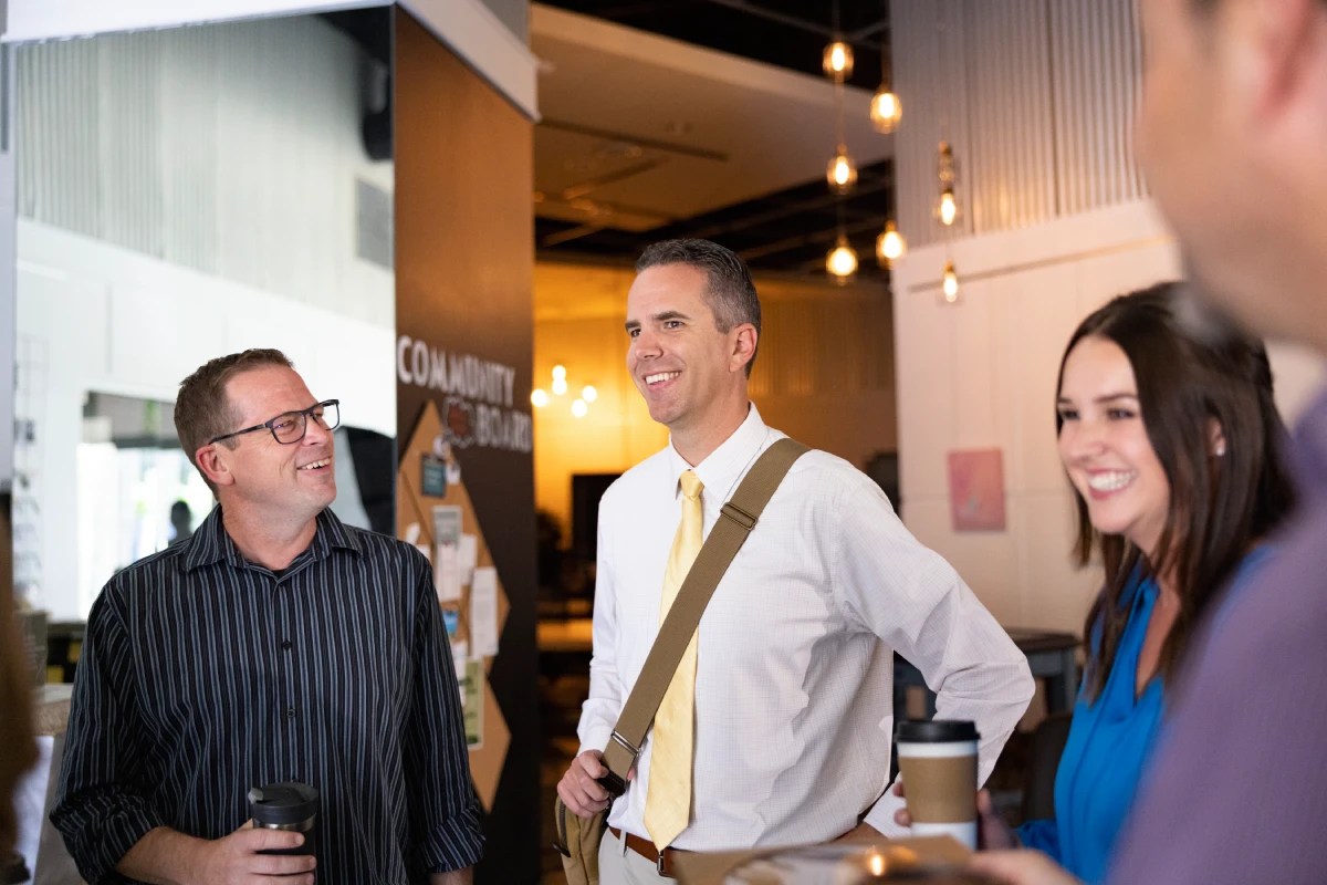 Group of people smiling and talking while holding coffee cups in an office setting