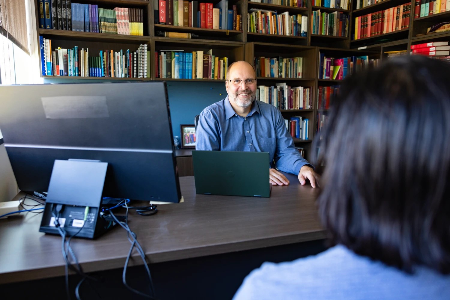 Professor meeting with a student in his office lined with bookshelves