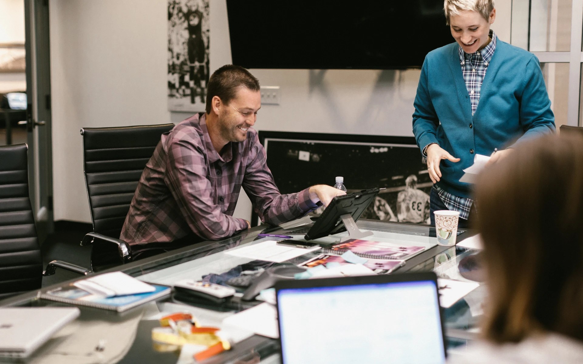 Two professionals smiling and collaborating during a meeting at a conference table with laptops and notes