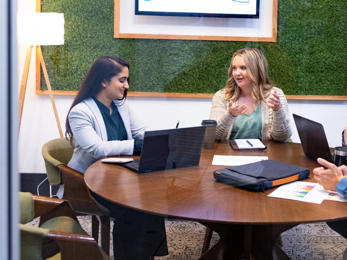 Two people sit at a round table with laptops and documents discussing data in a modern meeting room at Concordia University Irvine