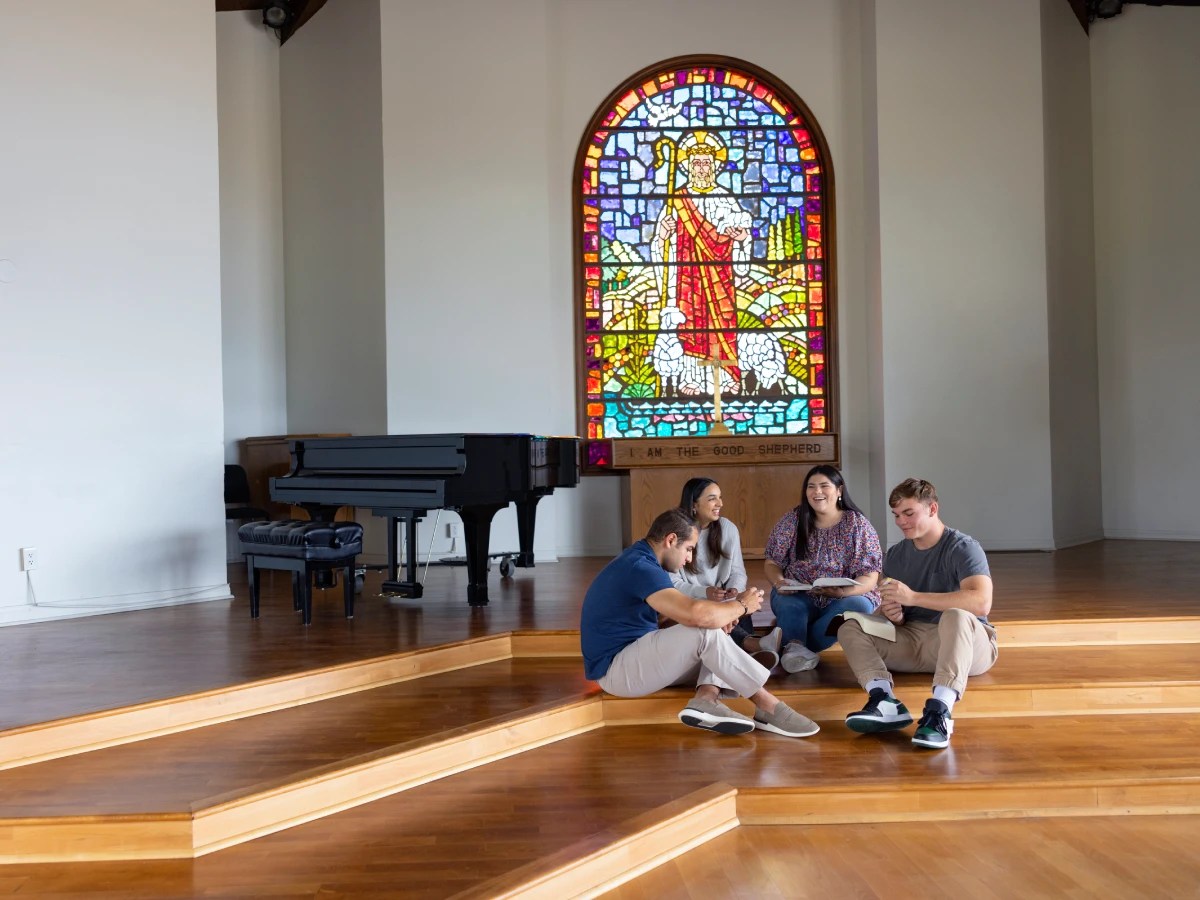 Students sitting together inside a chapel at Concordia University Irvine near a stained glass window depicting Jesus as the Good Shepherd