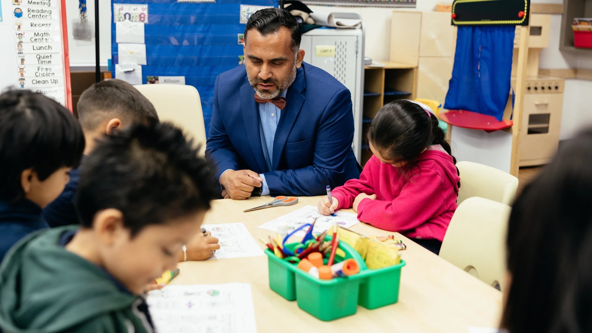 Teacher sitting with young students as they work on assignments at a classroom table