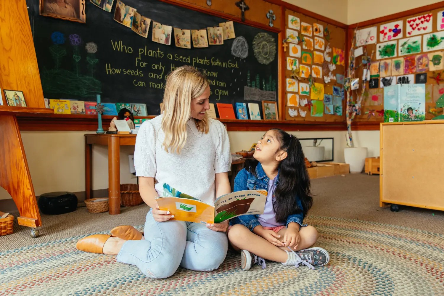 Teacher sitting on the floor reading a picture book with a young student in a classroom