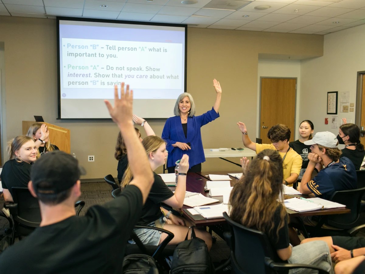 College students raising their hands during an interactive classroom activity led by a professor at Concordia University Irvine