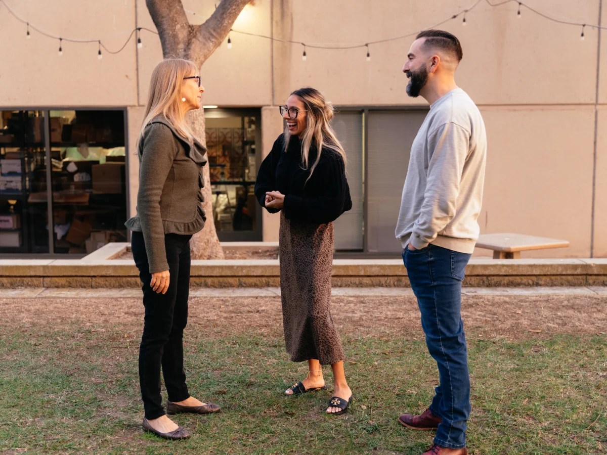 Three people stand outside a campus building having a friendly conversation at Concordia University Irvine