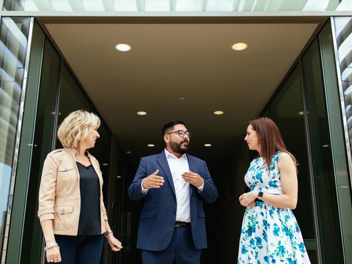 Three people stand outside a building entrance engaged in conversation at Concordia University Irvine
