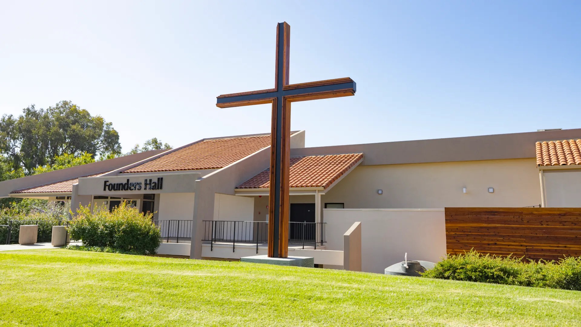 Large wooden cross in front of Founders Hall at Concordia University Irvine under a clear blue sky