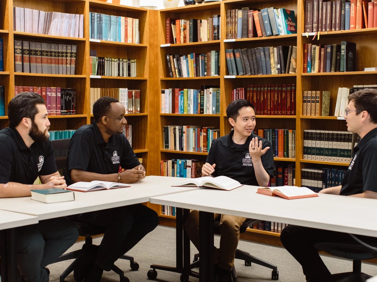 Group of ministry students in black Concordia University Irvine shirts studying and discussing books in a library