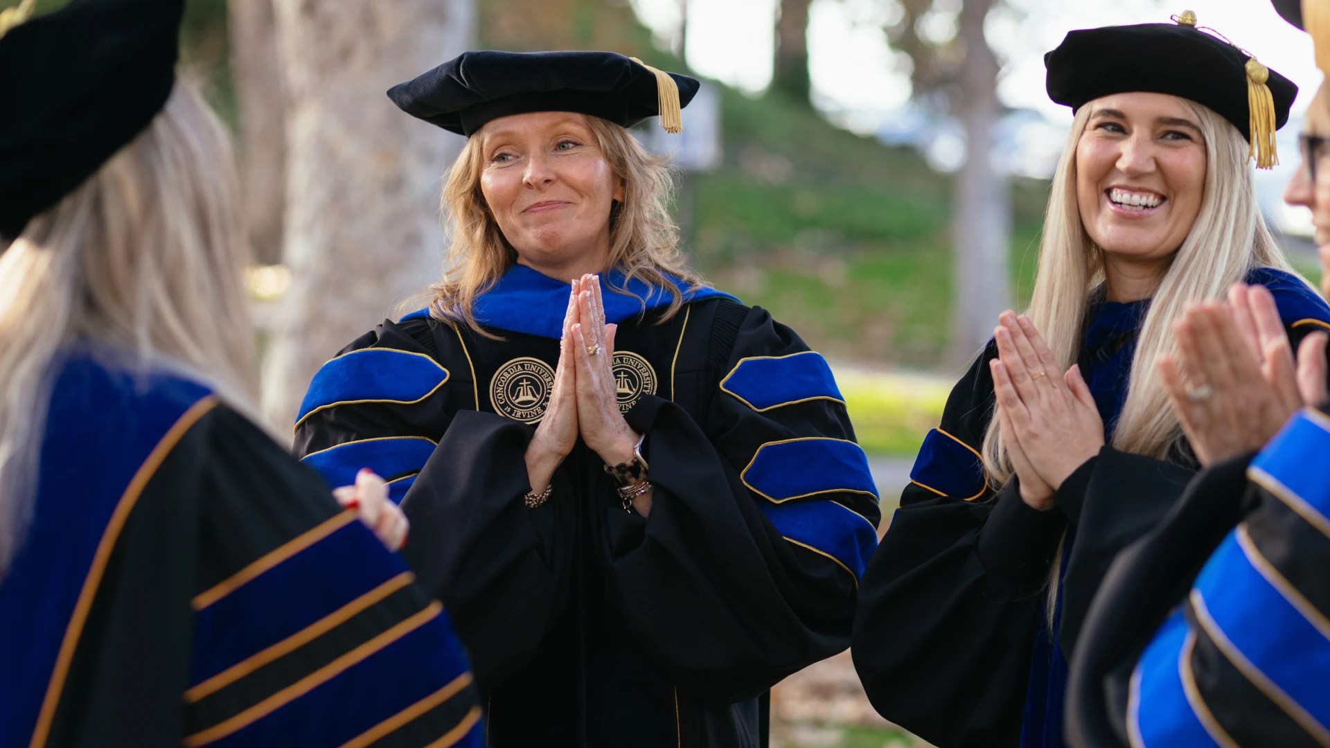 Faculty members in academic regalia smile and clap during a graduation ceremony at Concordia University Irvine