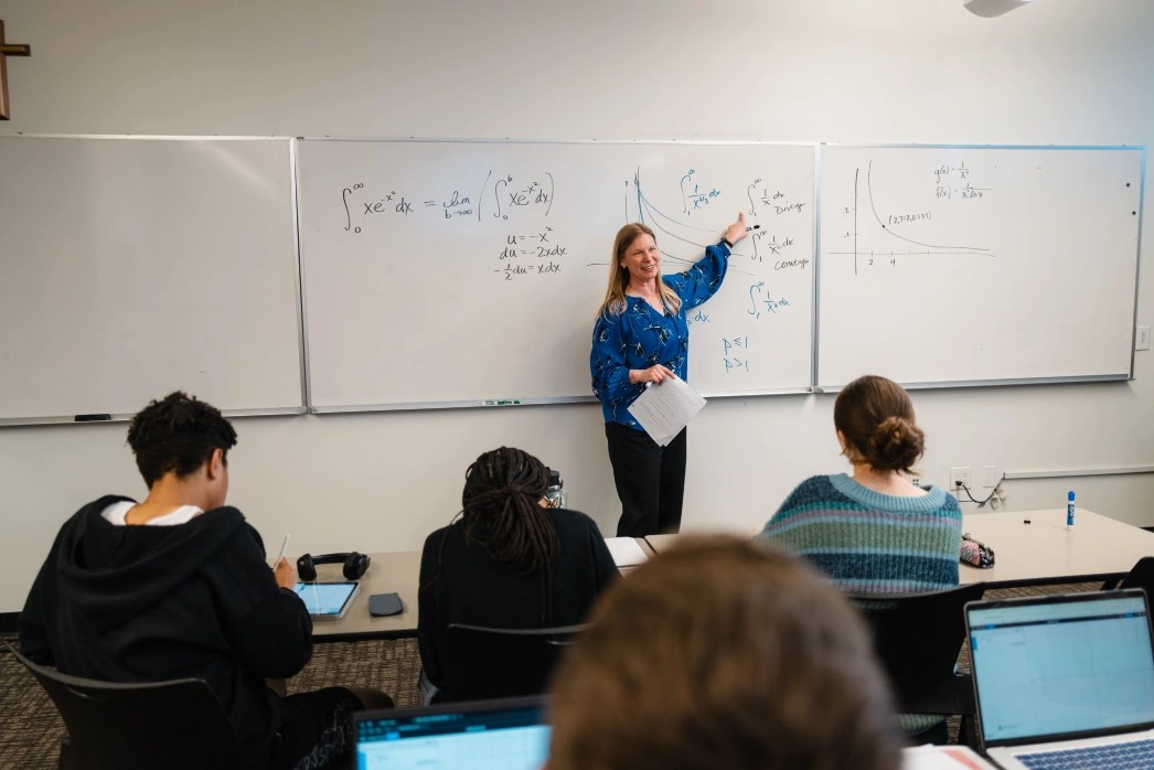 Professor standing at the whiteboard and teaching while students take notes in class