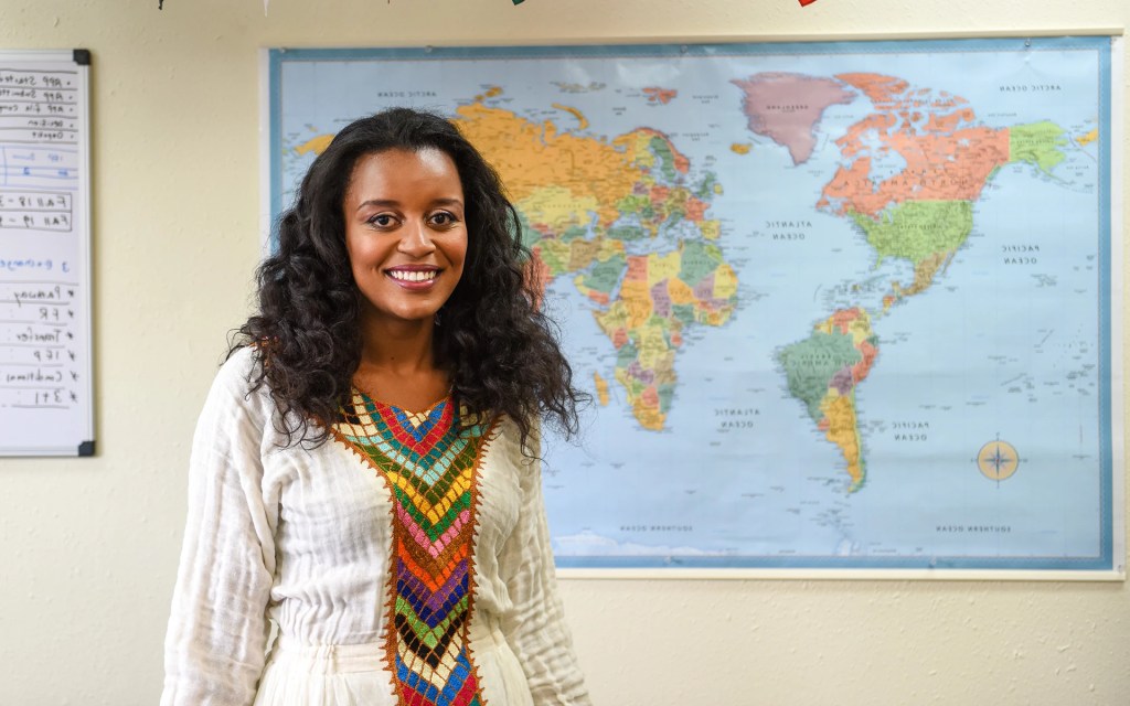 A student stands in front of a large world map in a classroom, smiling confidently at Concordia University Irvine
