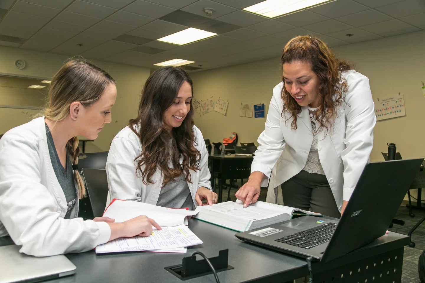 Instructor guiding two students as they review notes and textbooks together in classInstructor guiding two students as they review notes and textbooks together in class