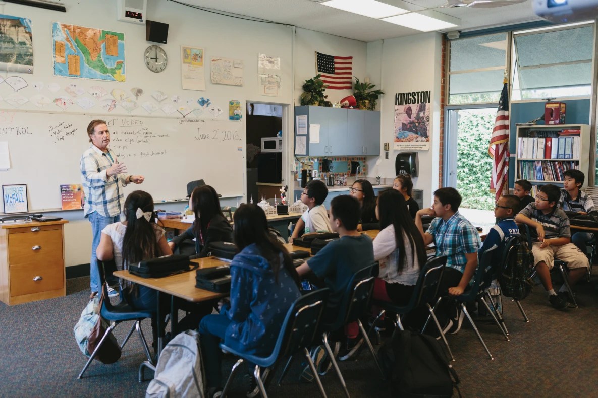 Teacher speaking to a classroom full of students seated at desks during a lesson