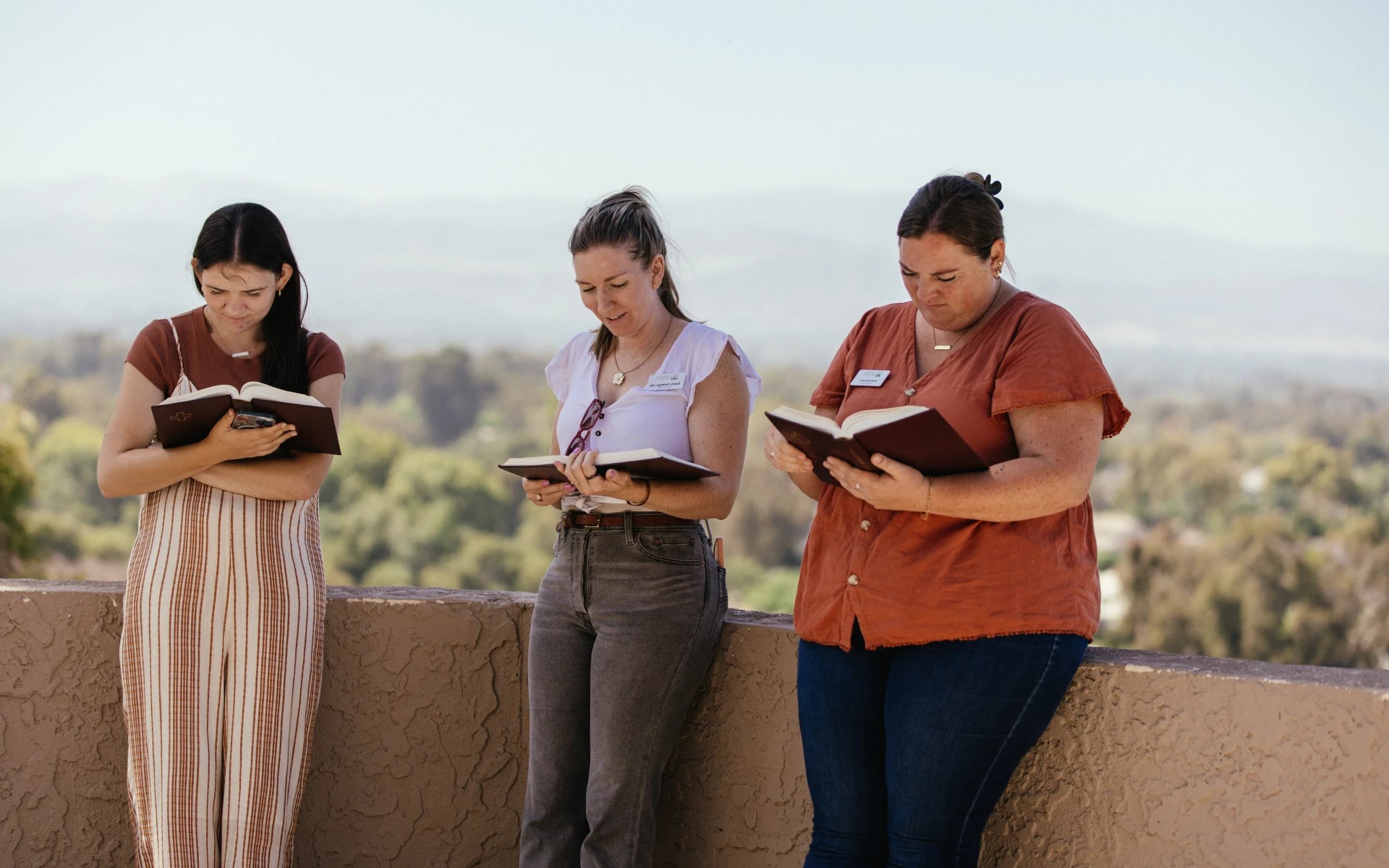 Three women from Concordia University Irvine reading their Bibles outdoors with a scenic view in the background
